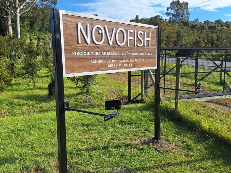 Novofish — Letrero de Alucom revestido con lamina HPL diseño madera, con logotipo volumétrico de PVC espumado, textos en vinilo adhesivo y borde de acero inoxidable
