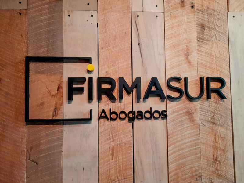 Firmasur — Logo Volumétrico pegado en pared de madera.
