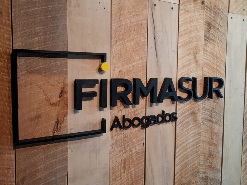 Firmasur — Logo Volumétrico pegado en pared de madera.