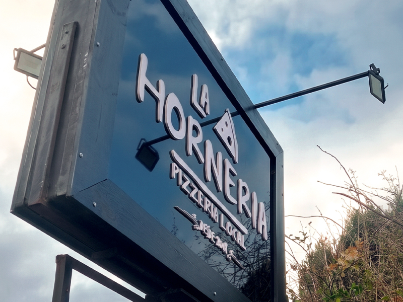 La Hornería — Letrero de alucom negro con logo volumétrico, instalado en estructura existente.